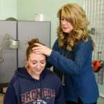 Woman with blonde wavy hair examining child's head in medical office setting
